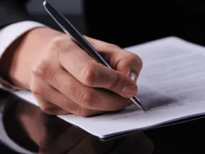 Personne en train de rédiger et signer des formalités administratives sur un bureau.