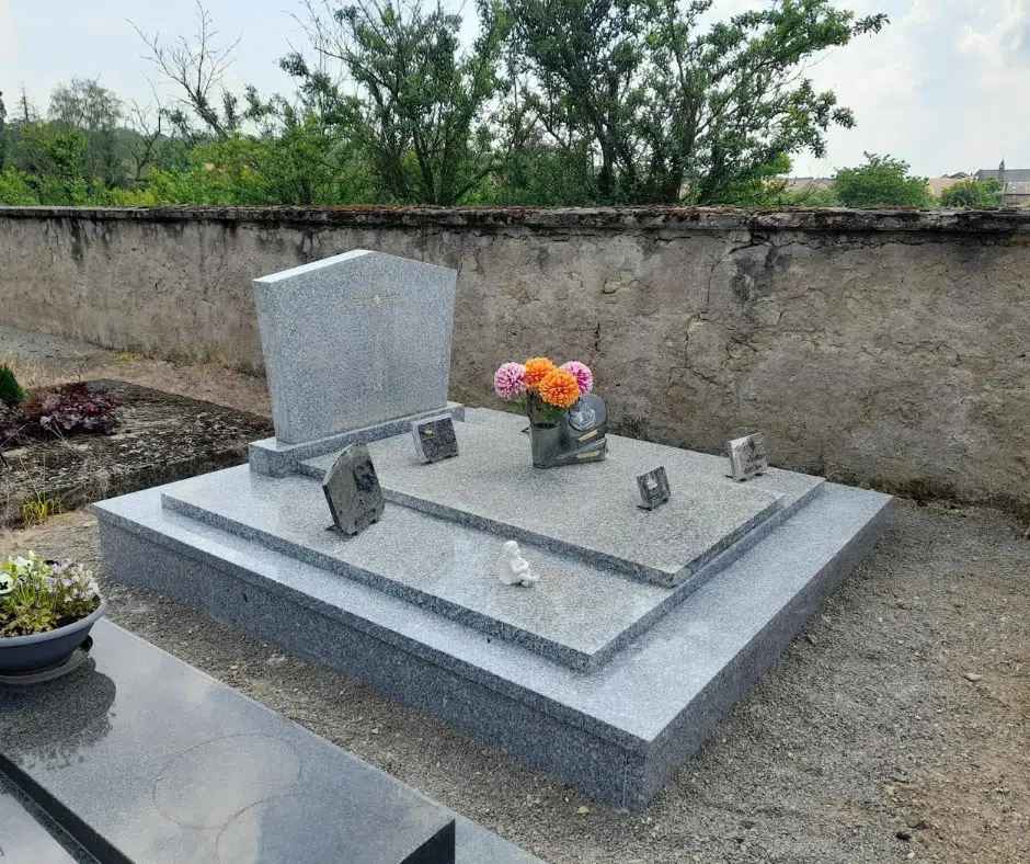 Pierre tombale en granit gris surmontée de plaques souvenir et d'un bouquet de fleurs