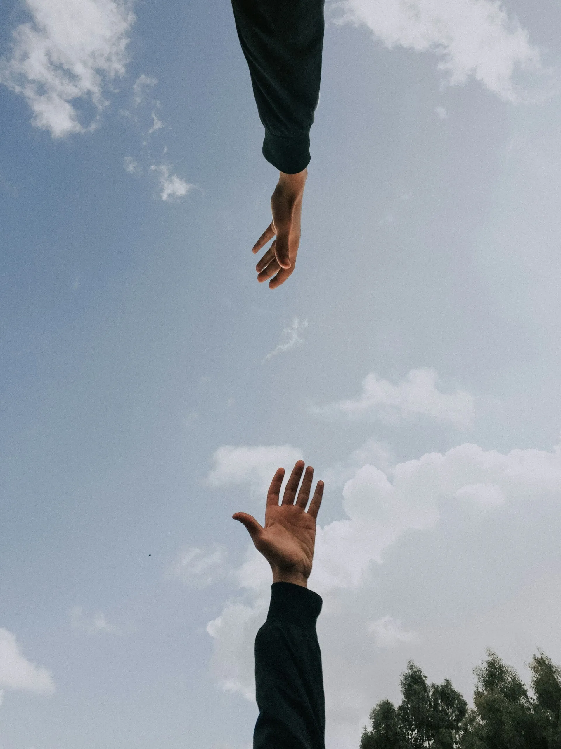 Deux mains tendues l'une vers l'autre sur fond de ciel bleu et nuages